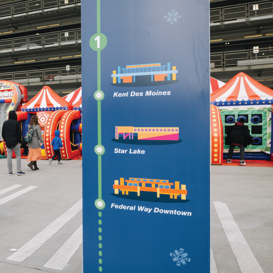 Sound Transit station totem listing Kent Des Moines, Star Lake, and Federal Way Downtown stops, with carnival tents behind it