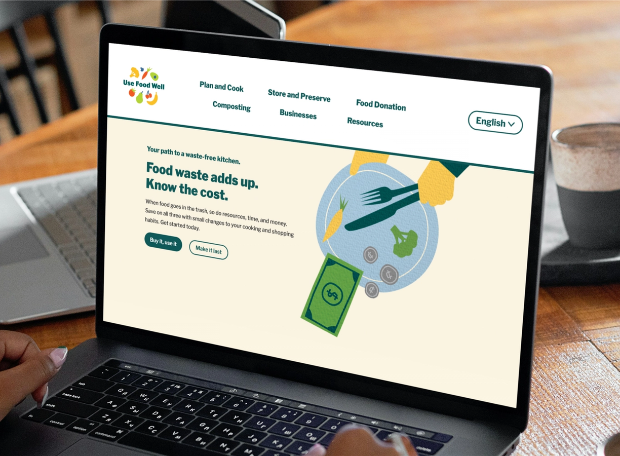 Laptop displaying the Use Food Well homepage reading "Food waste adds up. Know the cost." on a kitchen table