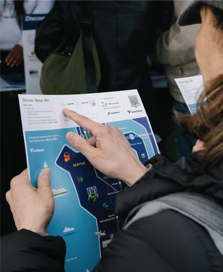 Woman pointing to 'discover, stamp, win' section of Federal Way Extension promo map