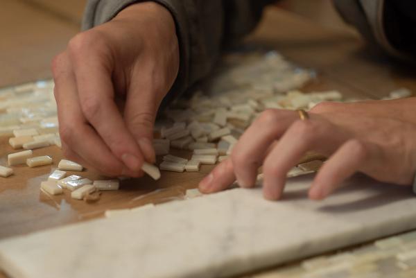 Mans col·locant tessel·les blanques sobre una peça de marbre.