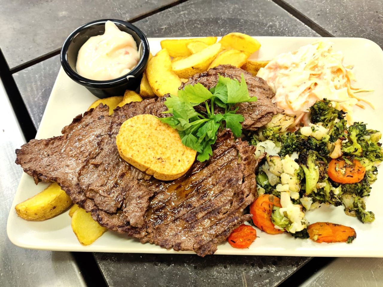 Plated steak with seasoned butter, golden potatoes, broccoli and carrots