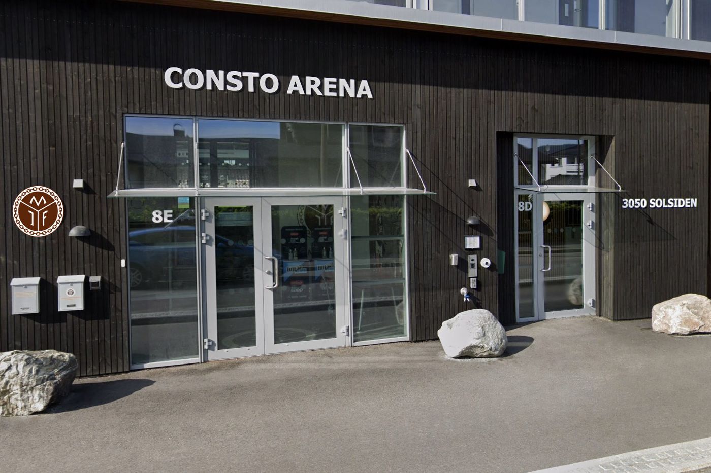 Inngangen til Consto Arena i Mjøndalen, en mørk trefasade med Mjøndalen IFs logo ved døra.