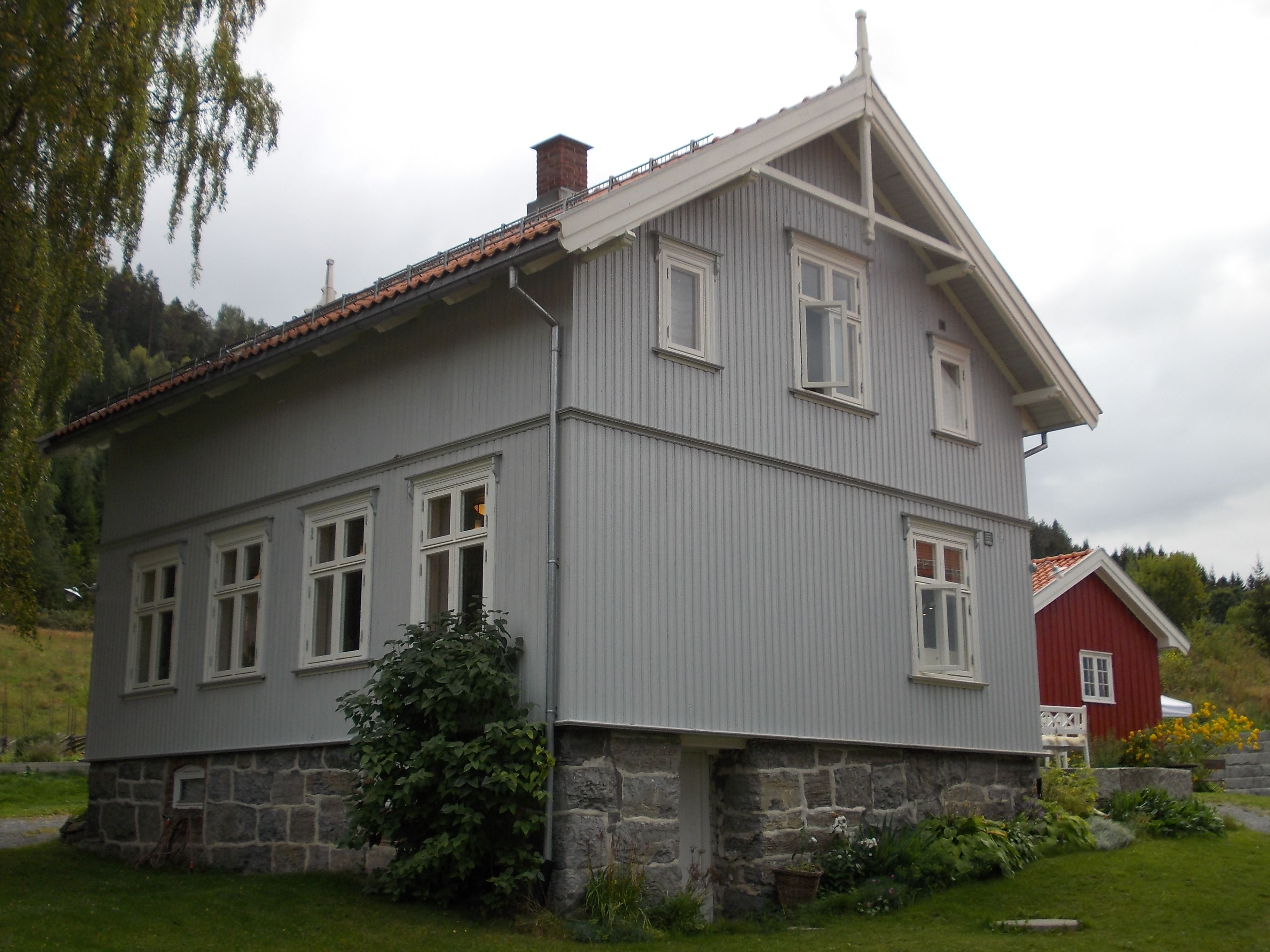 Hovedhuset på Portåsen, et grått trehus i to etasjer med hage foran og et rødt uthus i bakgrunnen.