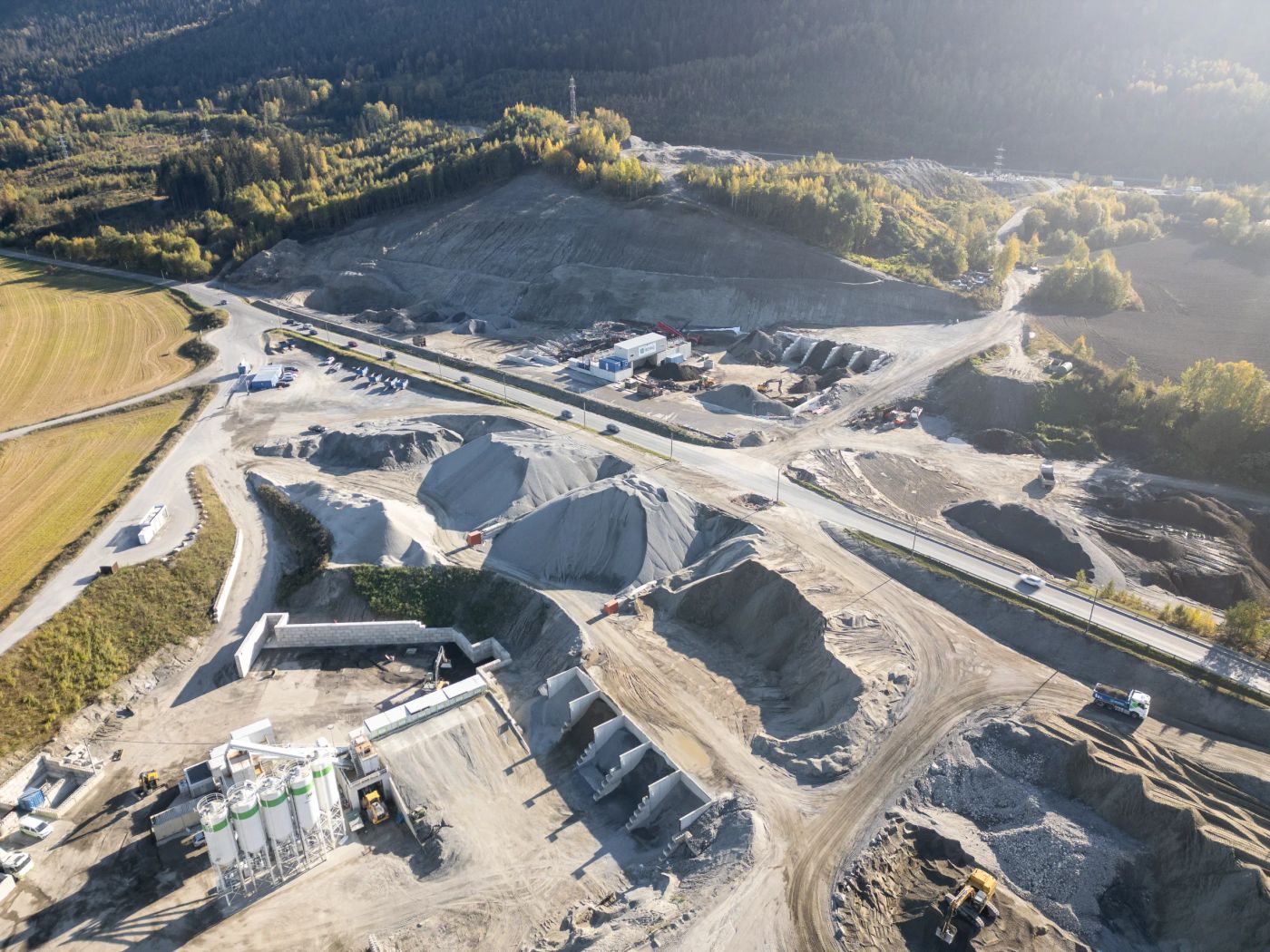 Dronefoto av masseuttaket en høstdag, med sandhauger og containere i forgrunnen og Drammenselva og dalen bak.