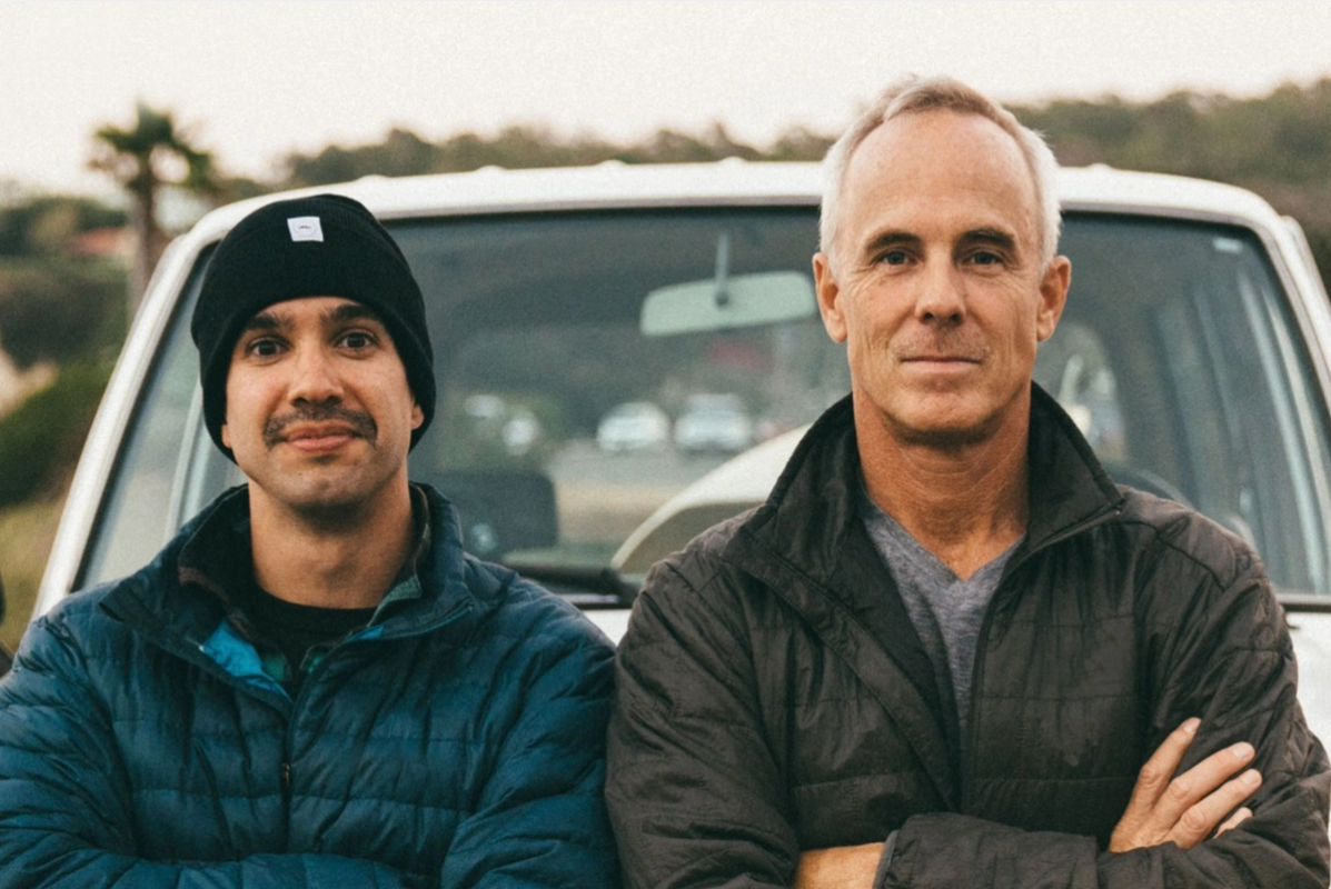 Two men standing in front of a white ute with their arms crossed looking at the camera