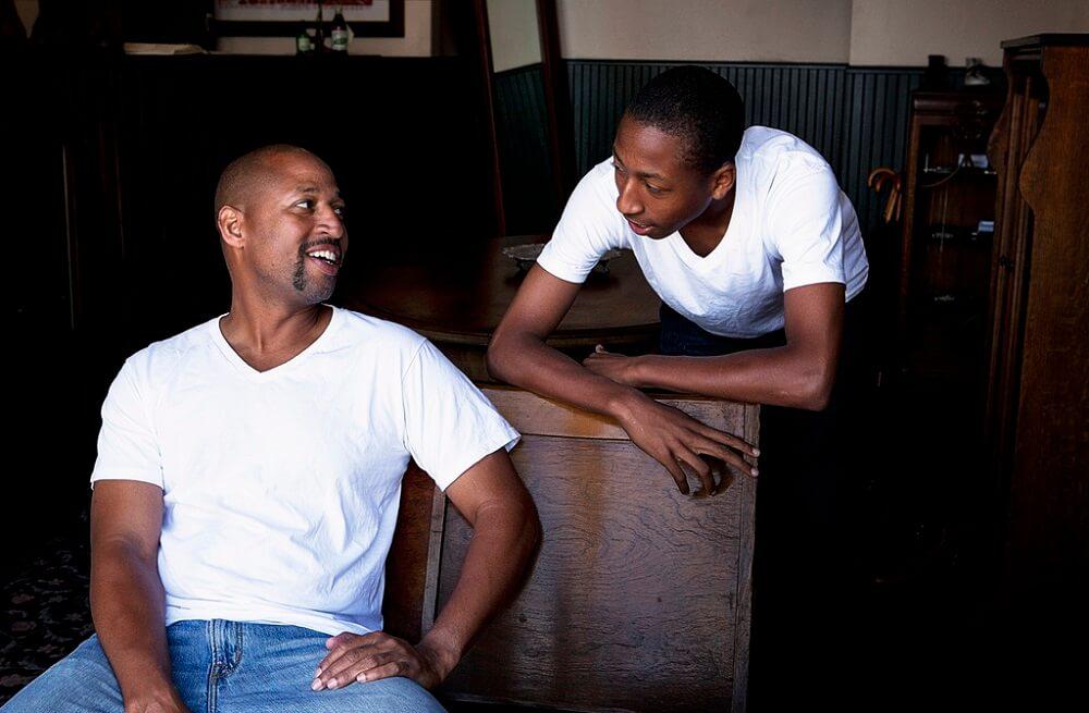 Two men smiling and talking together in a relaxed indoor setting.