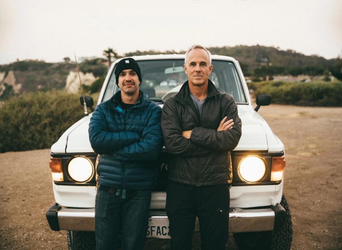 Two men standing together in front of a truck outdoors.