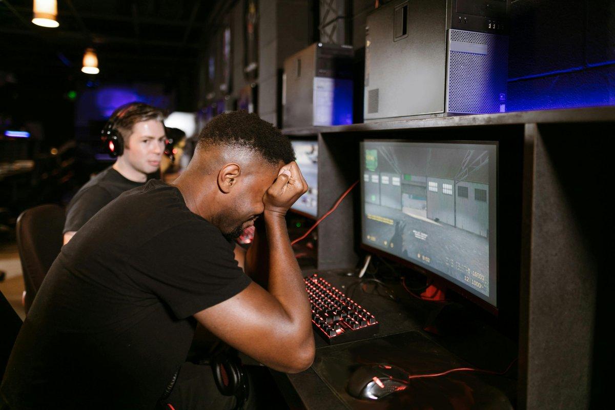 Frustrated gamer with head in hand at his PC while a teammate looks on in a dark esports arena