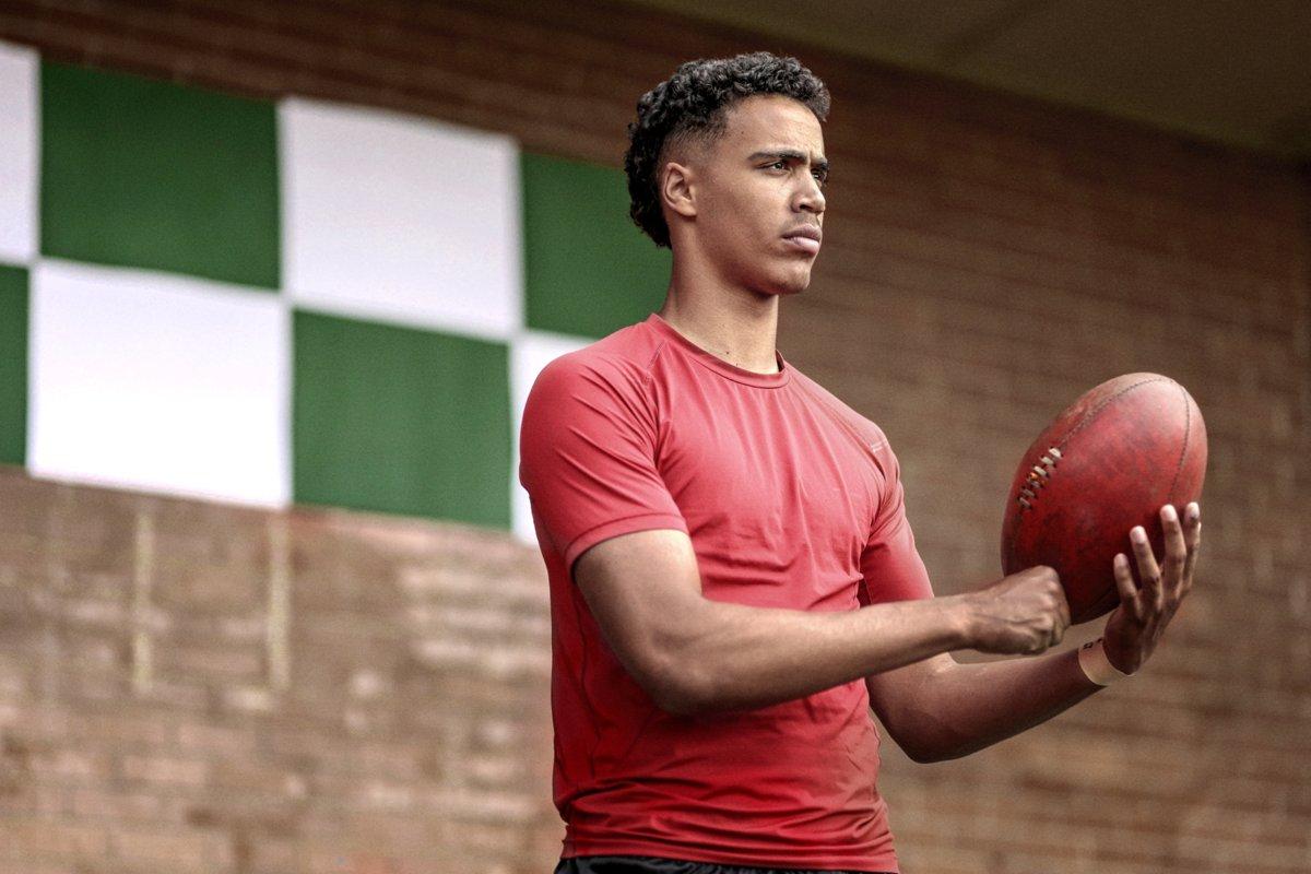 A young AFL player holding a football, focused and composed before play.