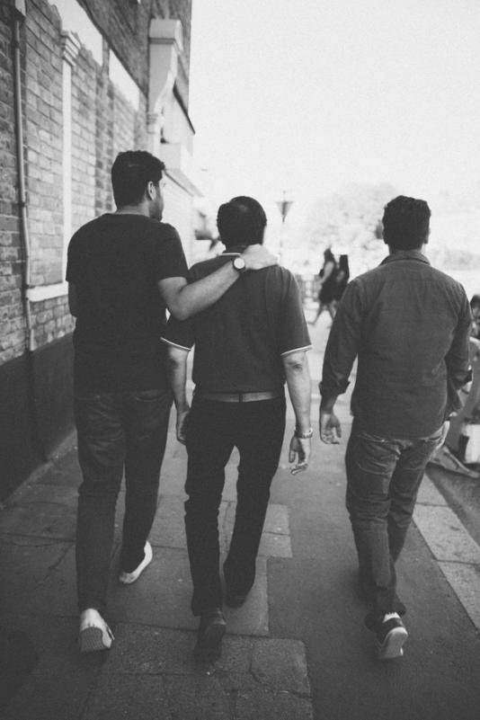 Three men are walking with their backs towards the camera and their arms around each other