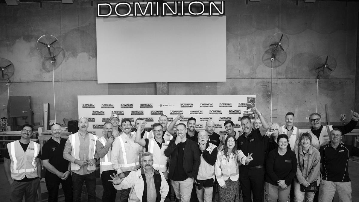 Black and white, team of construction workers pose in front of media wall at fundraising event.