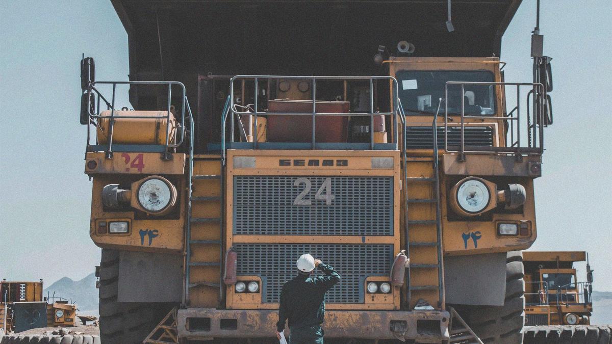 Photo of a man on a desert mining site, looking up to a large mining truck.