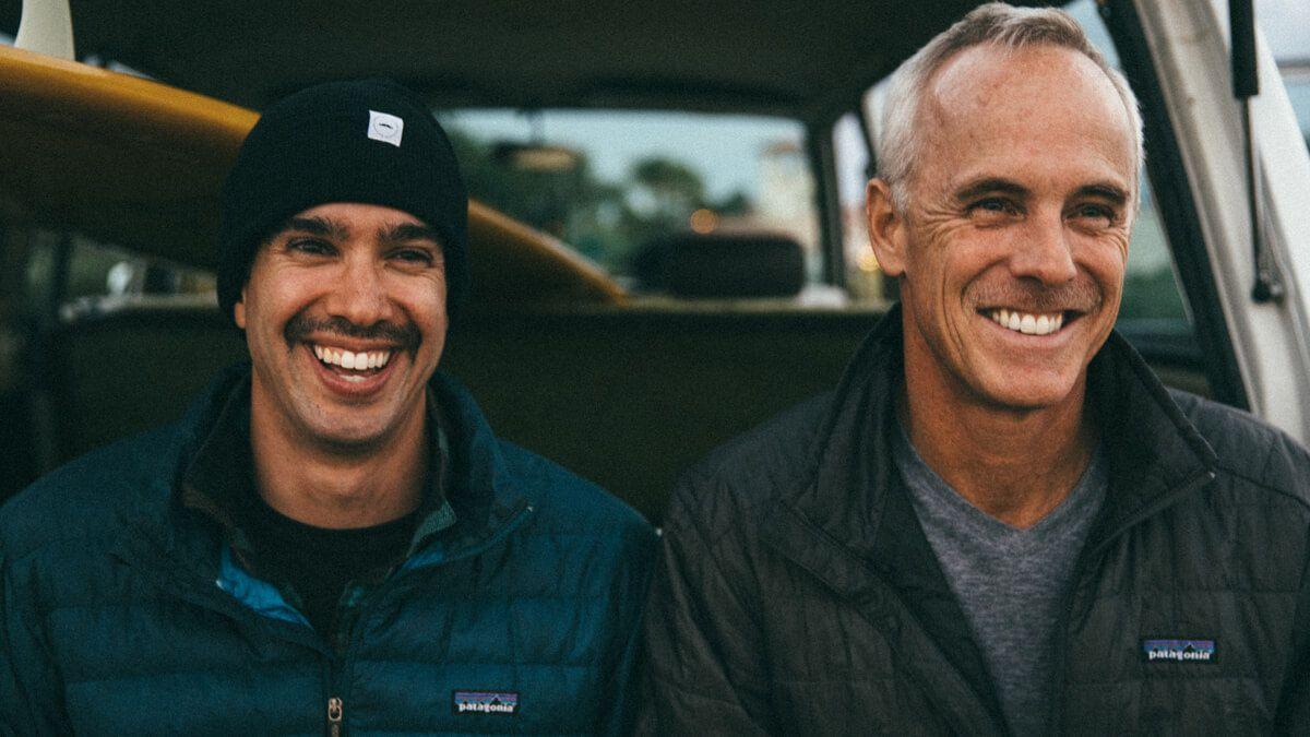 Close up of two men sitting against a car
