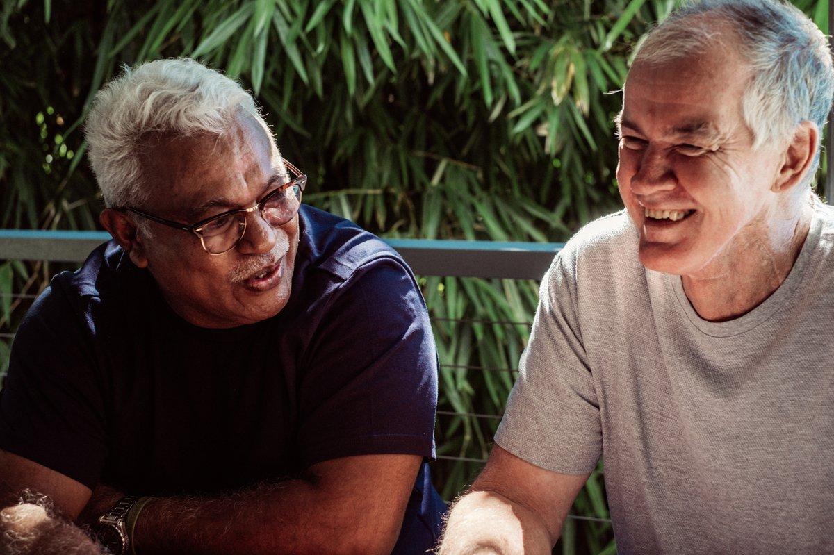 Two older men sitting together outdoors, laughing and talking.