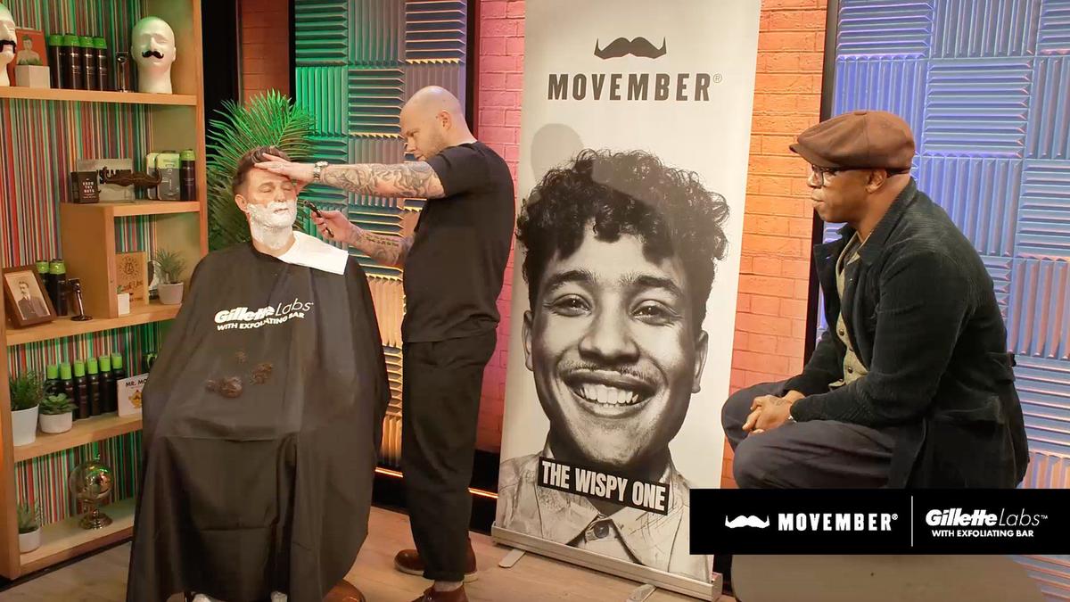 Ian Wright watches a man shave another man's face.