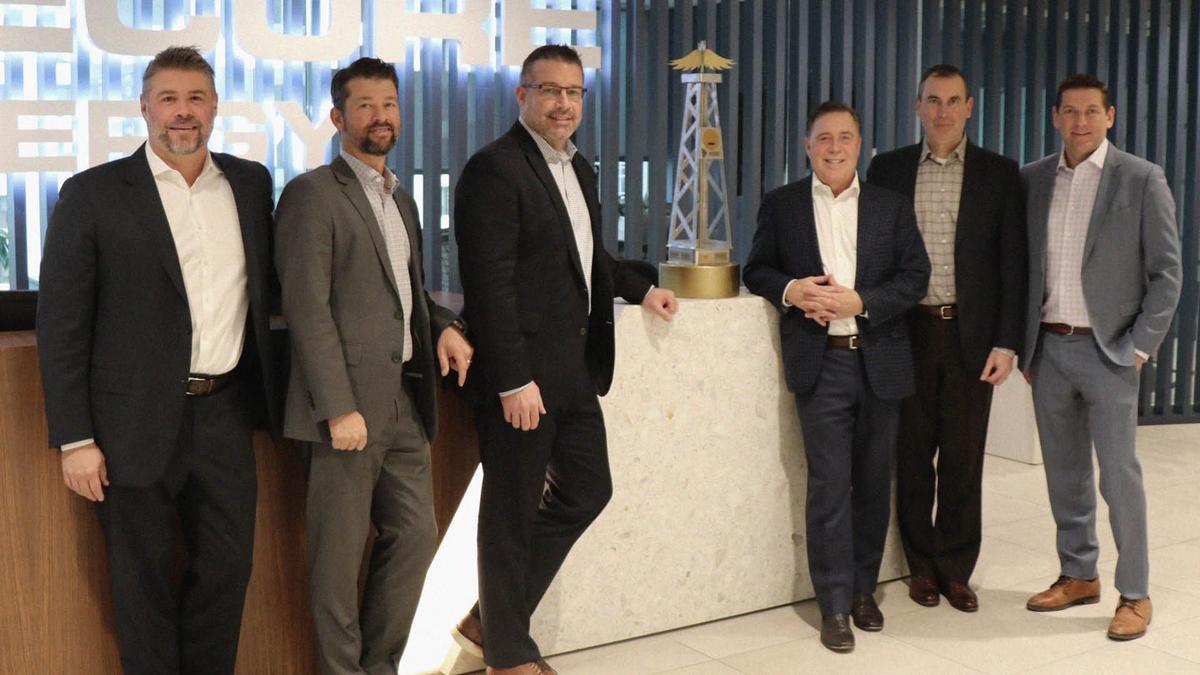 Group of men stand around a large trophy they wont for being the top team in the oil and gas sector