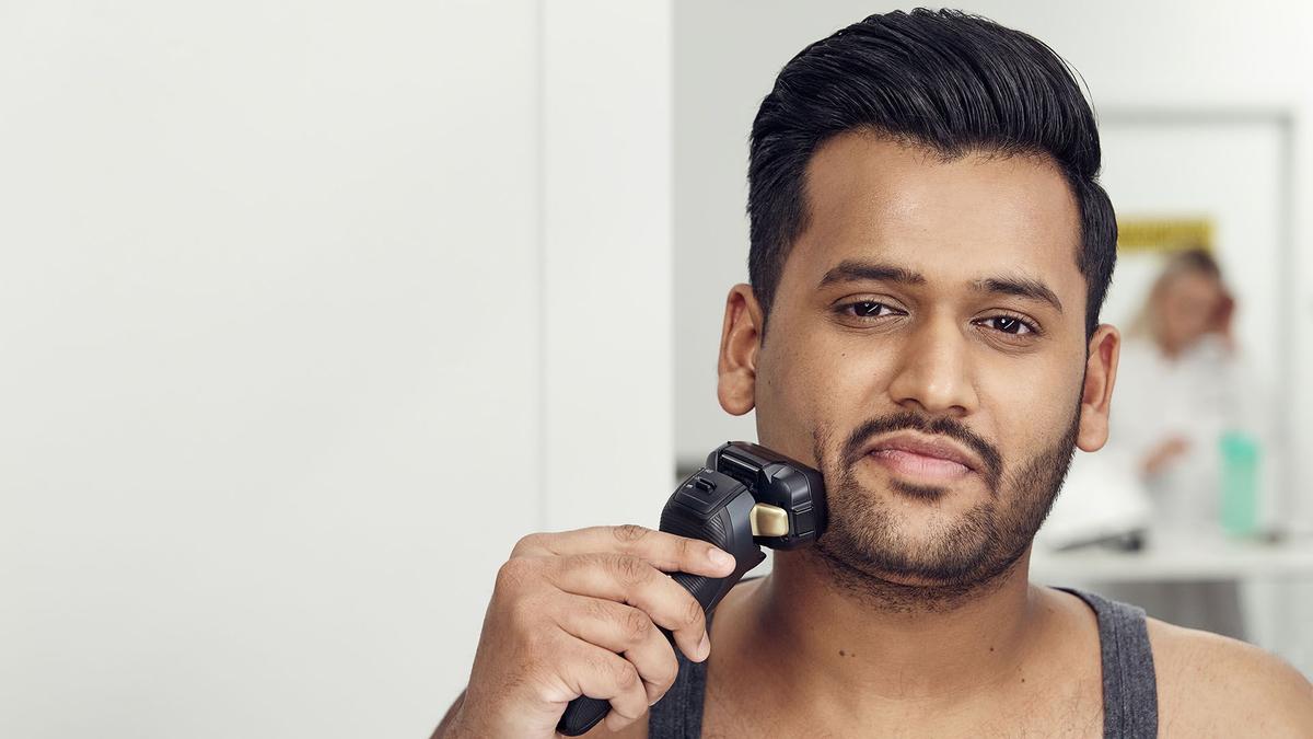 Photo of handsome man, looking to camera, shaving with an electric Panasonic razor.