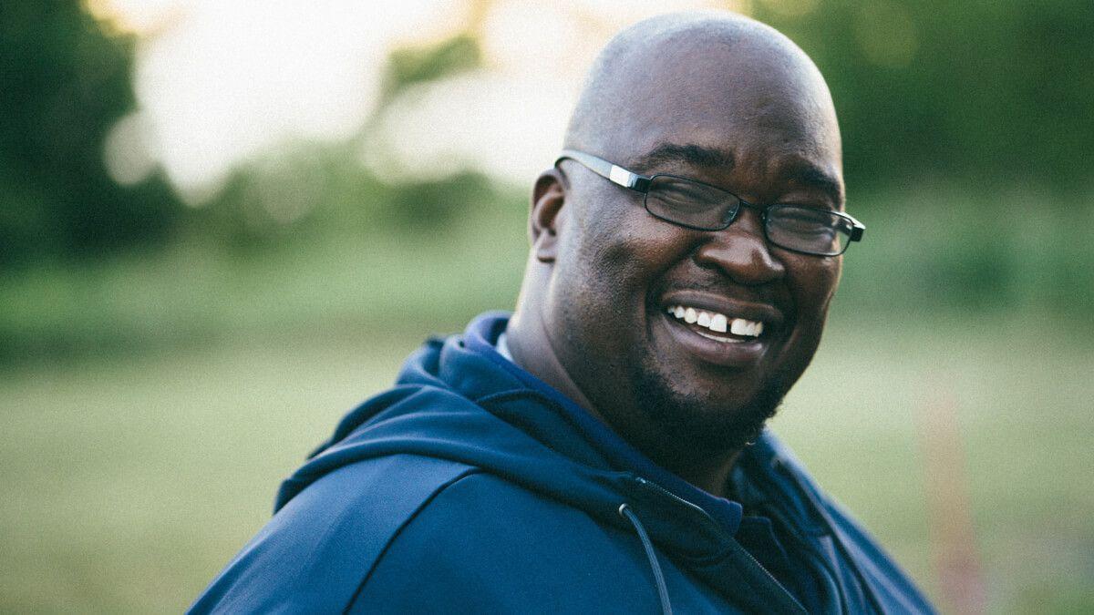 Black man wearing glasses and a blue hoodie top having a laugh