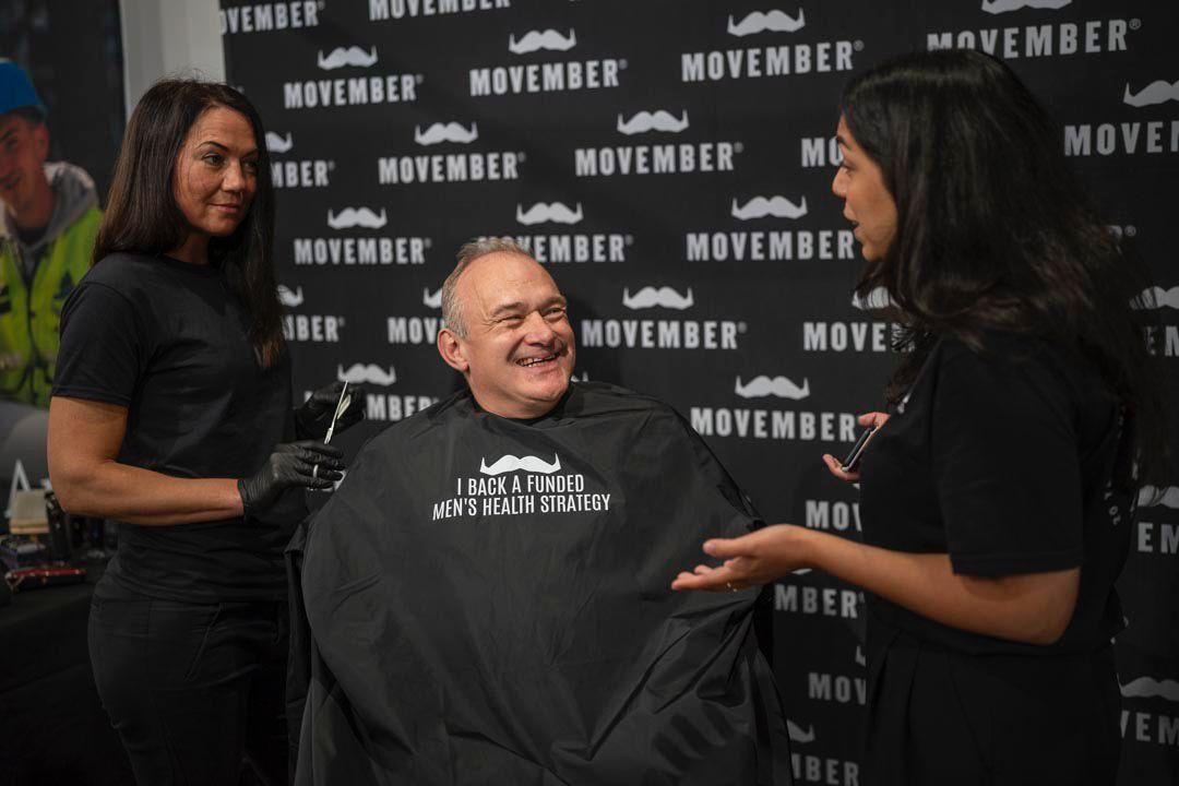 A man wearing a Movember barber gown is smiling at a Movember event