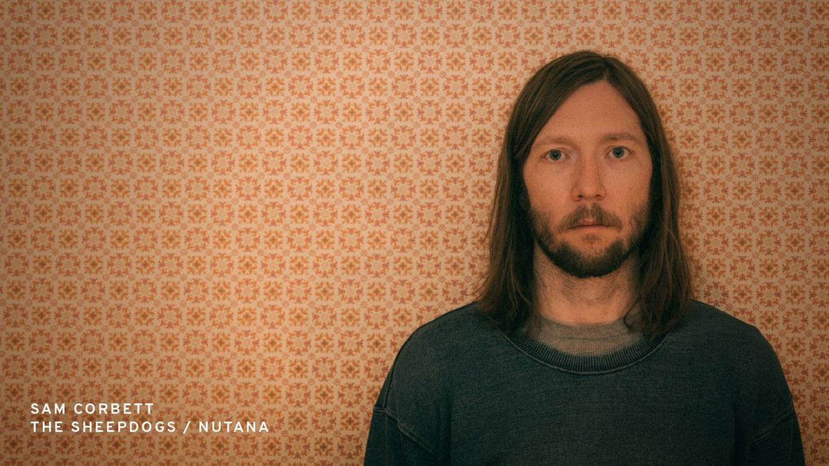 Sheepdogs drummer Sam Corbett poses in front of patterned wallpaper