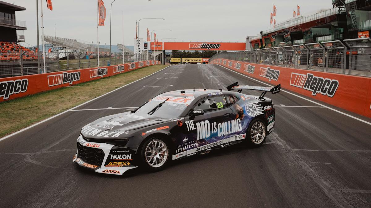 Racing car covered with Movember signage and messaging sits on Bathurst racing track.