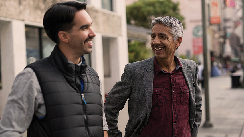 A father and son smiling at each other mid-conversation 