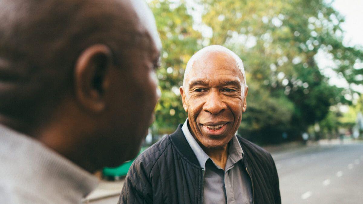 Two older Black men speaking to each other next to a road