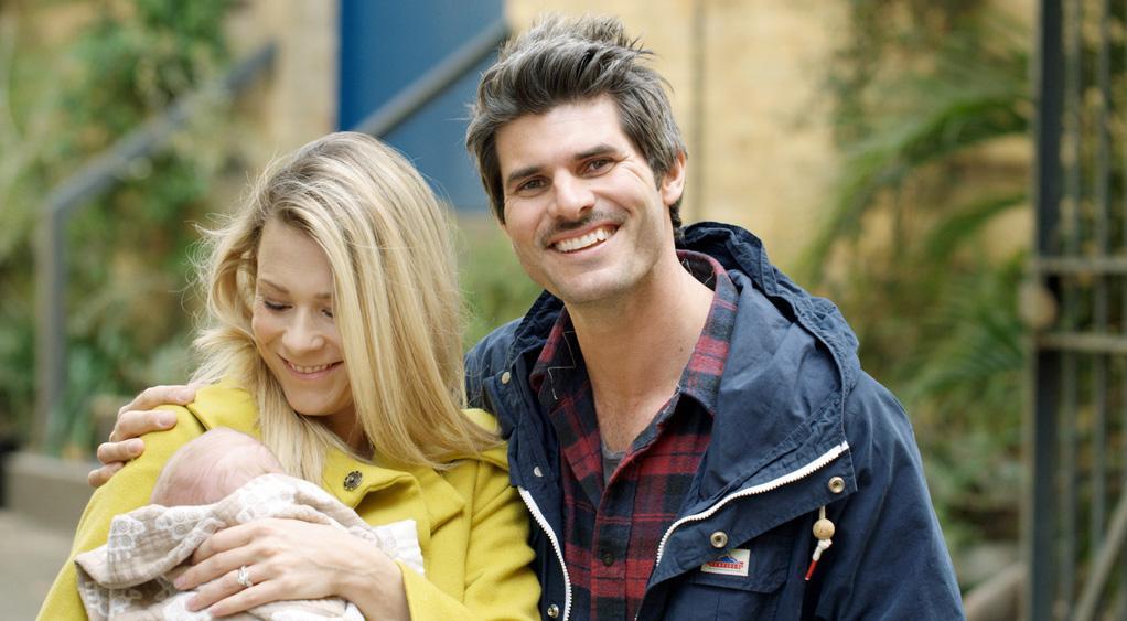 Mother and father with infant, smiling to camera.