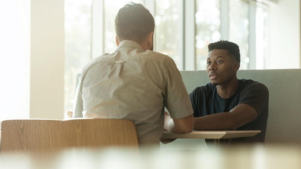 Two men sitting across from each other at a cafe table, having a conversation.