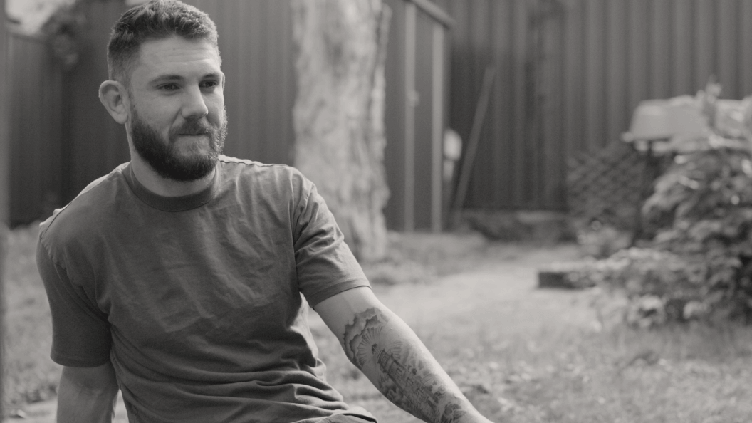 Man with beard and tattoo sitting in their backyard