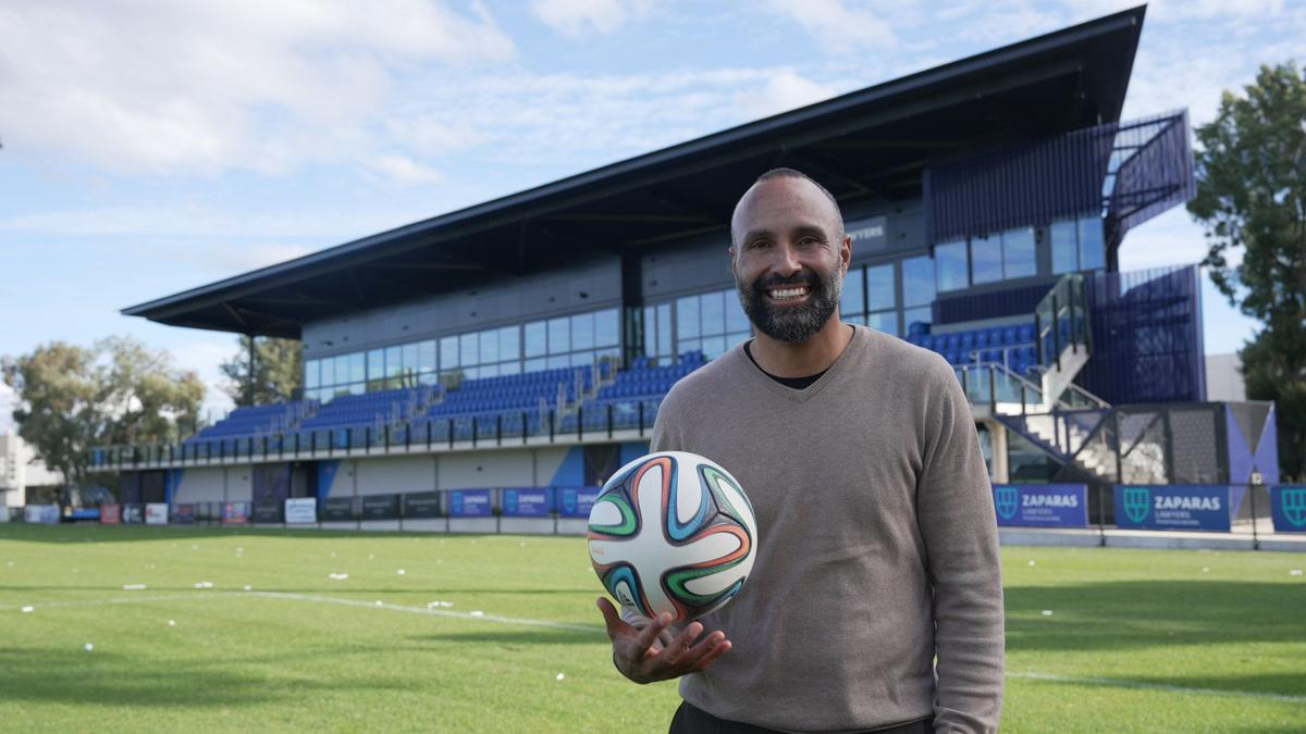 Man juggles football in hand standing in front of sports ground stand