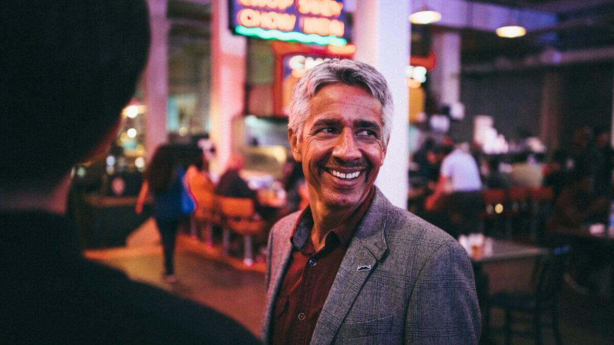 Older man in grey blazer and red shirt meeting people in a restaurant