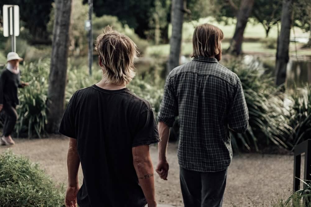 Two men walking side by side through a park, seen from behind.