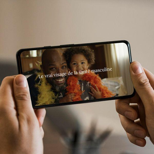 Photo of a phone, playing a video about the Real Face of Men's Health, with French text superimposed.