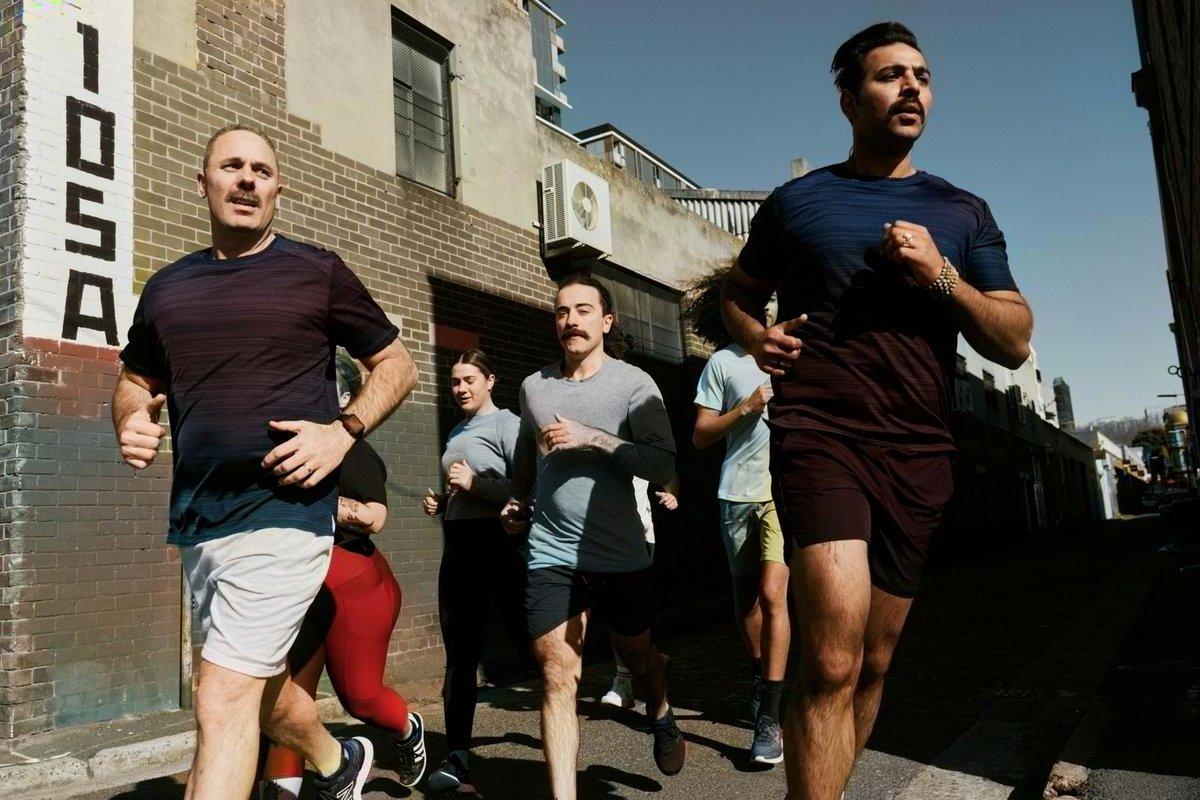 A group of men and women running together through an urban laneway on a sunny day.