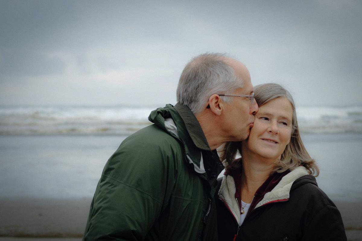 Older man kissing his female partner on the cheek on the beach