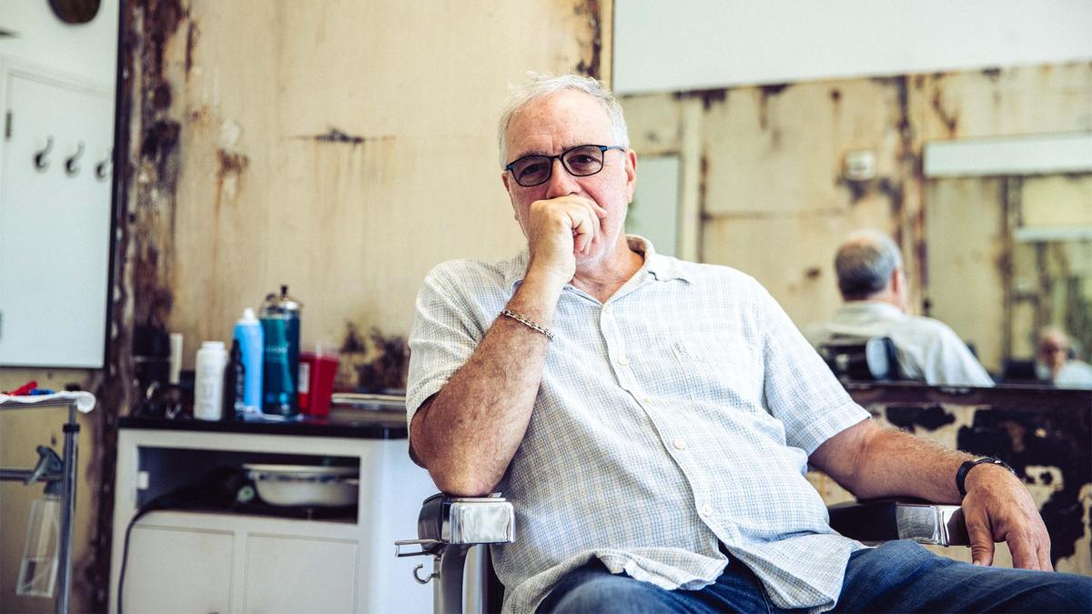 A man with glasses poses pensively from the barber chair of an LA barber shop