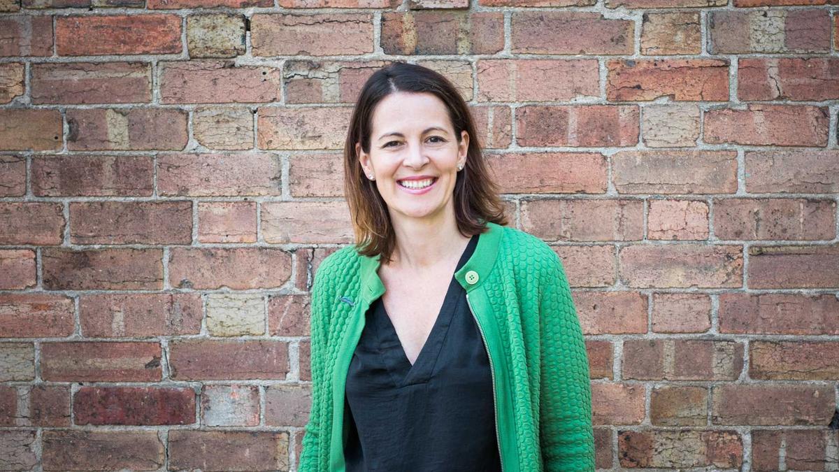 Lady stands in front of brick wall wearing green cardigan and black top