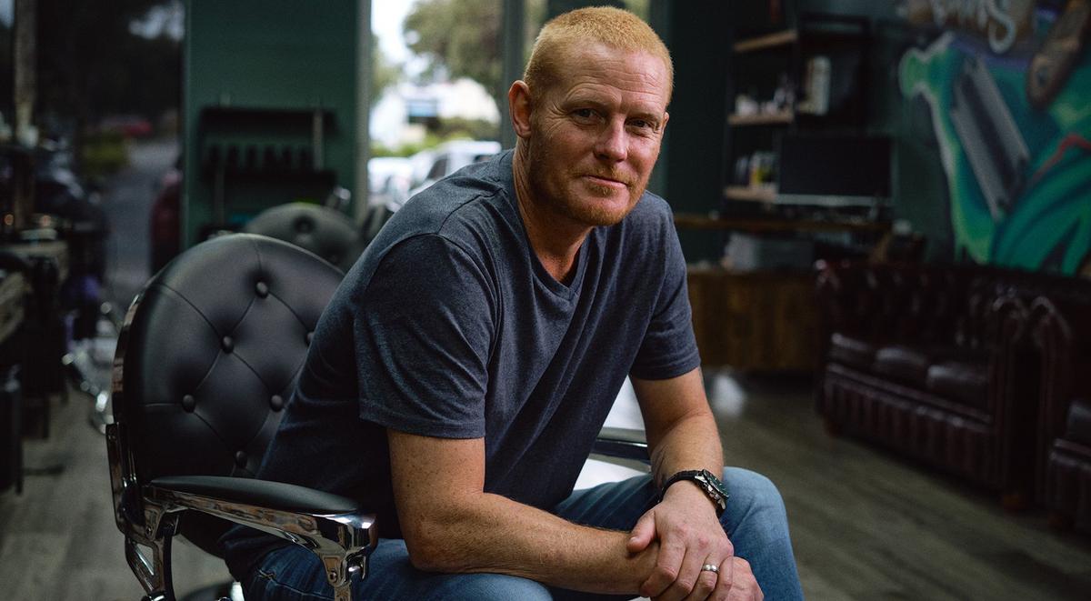 Seated man looking contemplative at camera from a barber chair.