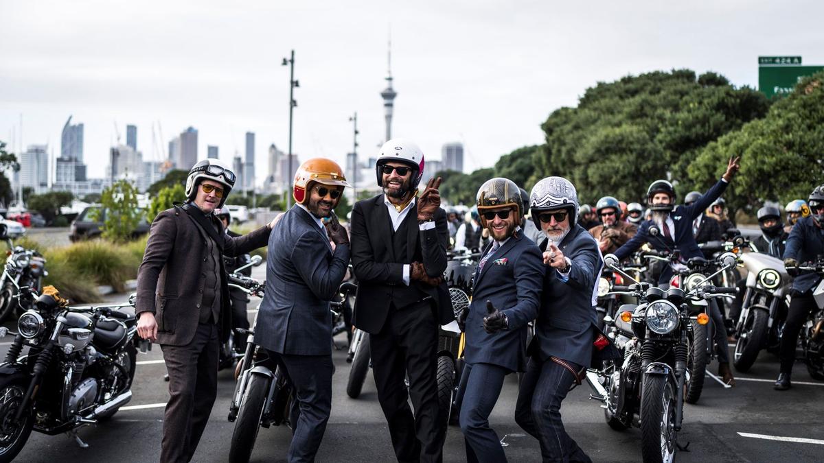 Five men in suits stand on road in front a motorbikes with Auckland skyline in the background including the sky tower