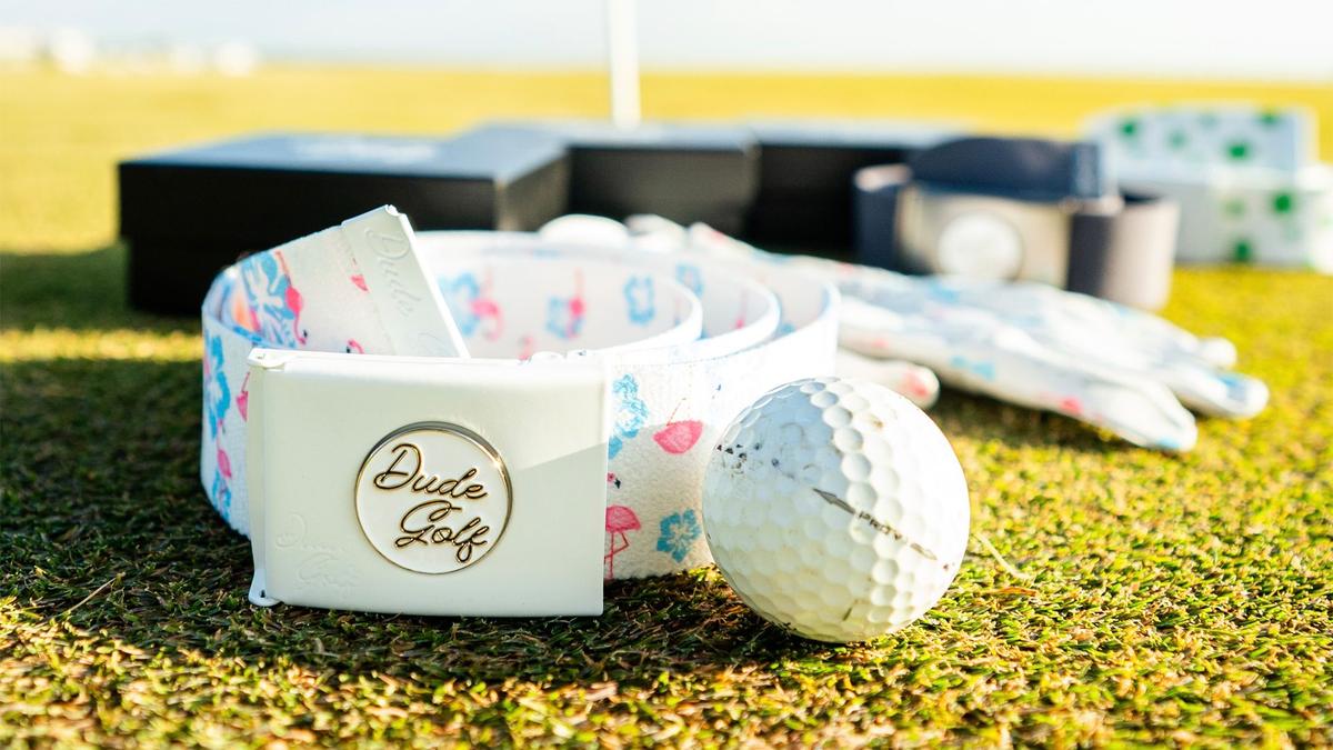 Product photo on golf green featuring a golf ball and belt buckle that reads Dude Golf