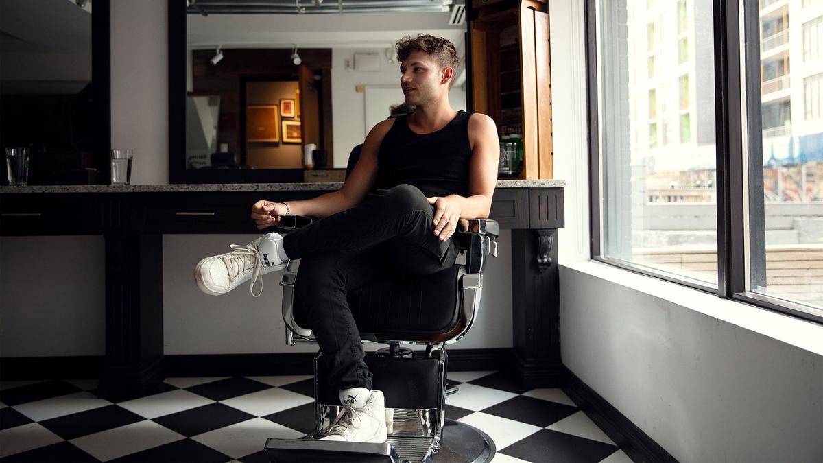 A young man sits casually in a barbershop with black and white checkered floors