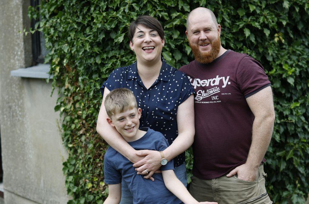 A young family have their arms around each other smiling