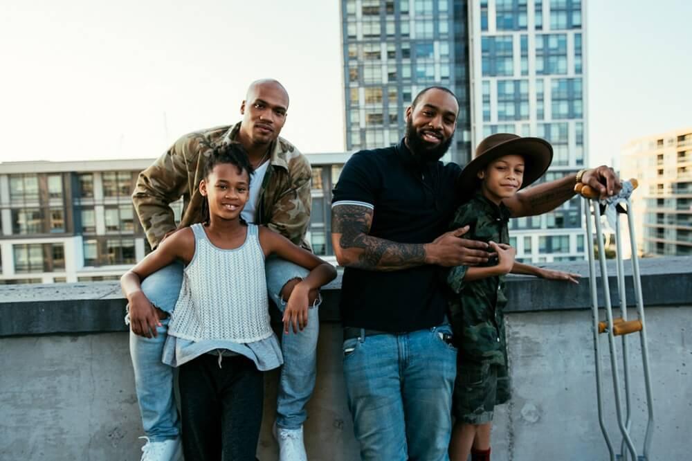 Two men with their children on a rooftop in the city.