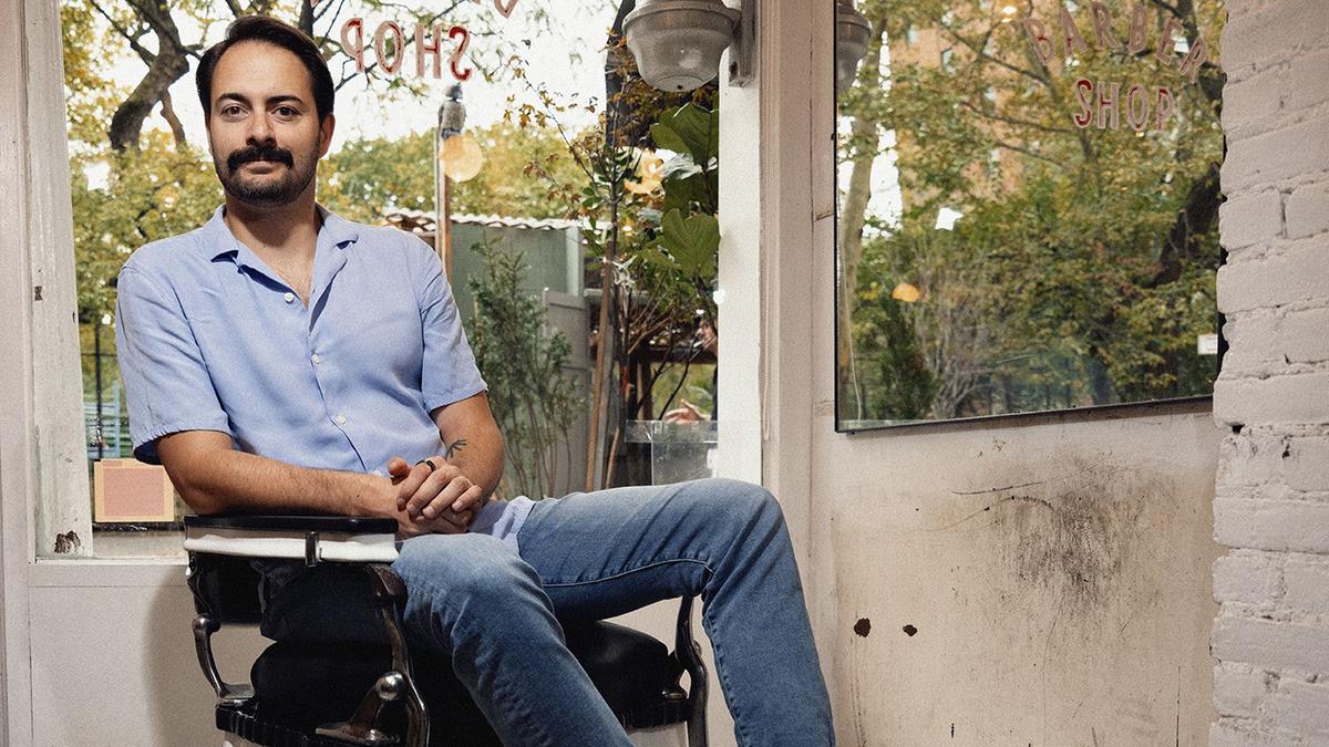 A man with a bushy black moustache poses in a barber chair