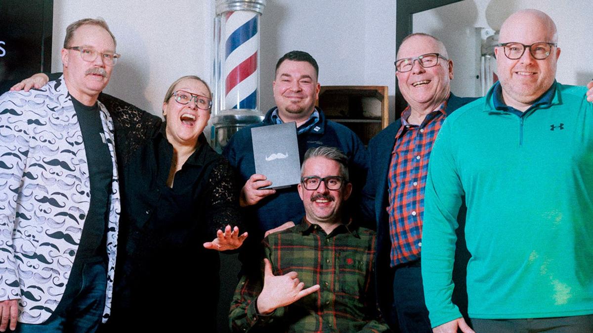 A group of people who have just won a Movember award pose for a portrait in a barbershop setting