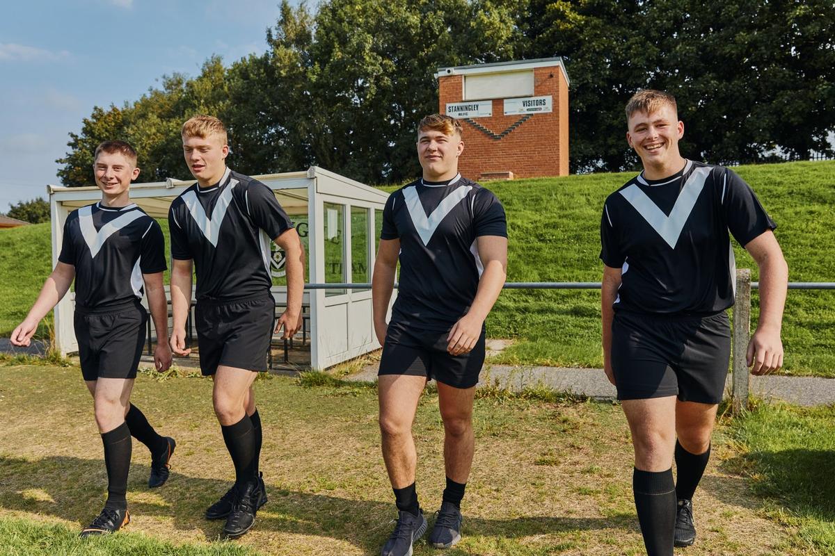Four teenage boys in football kit walking together at a rugby ground.
