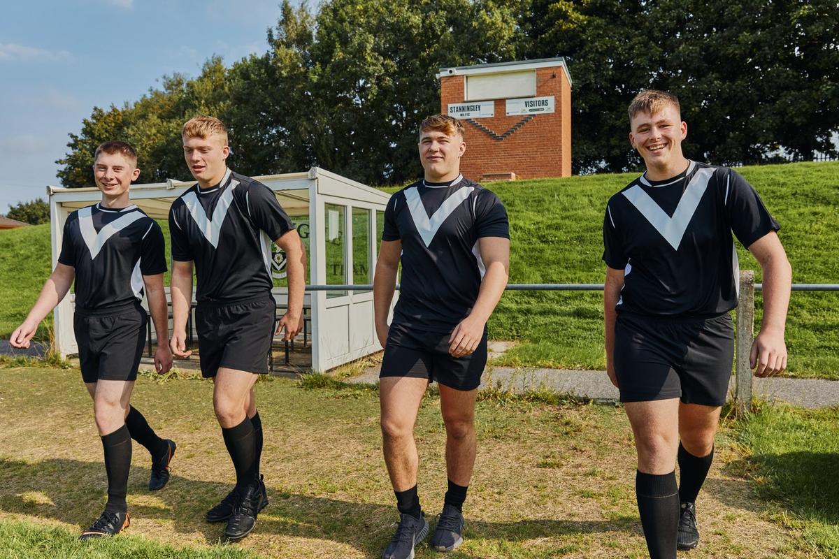 Four teenage boys in football kit walking together at a rugby ground.