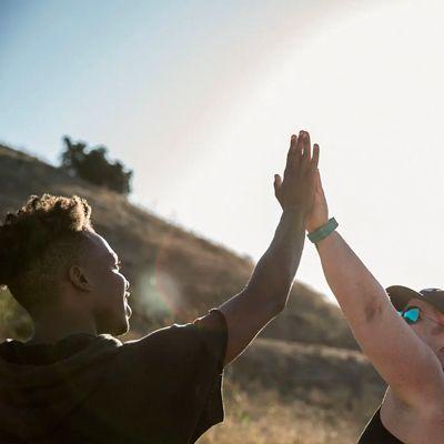 Two people high-fiving outdoors in bright sunlight against a hillside backdrop.