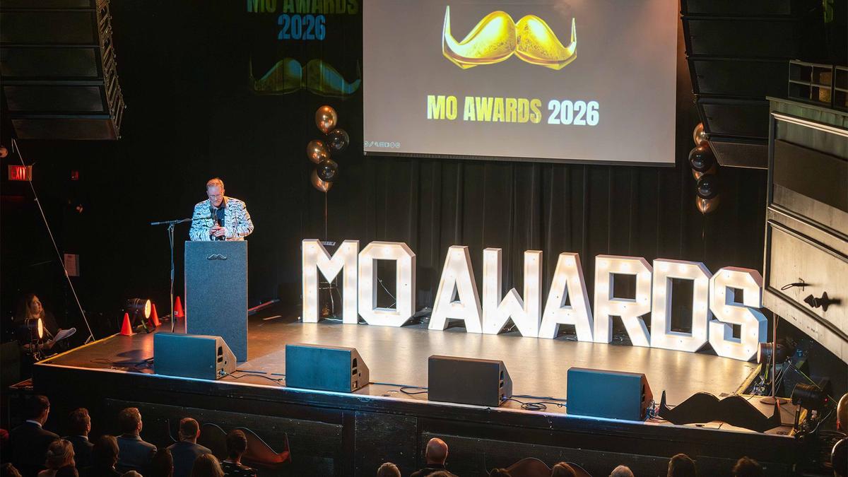 A man on stage with big lights on stage that say "Mo Awards"